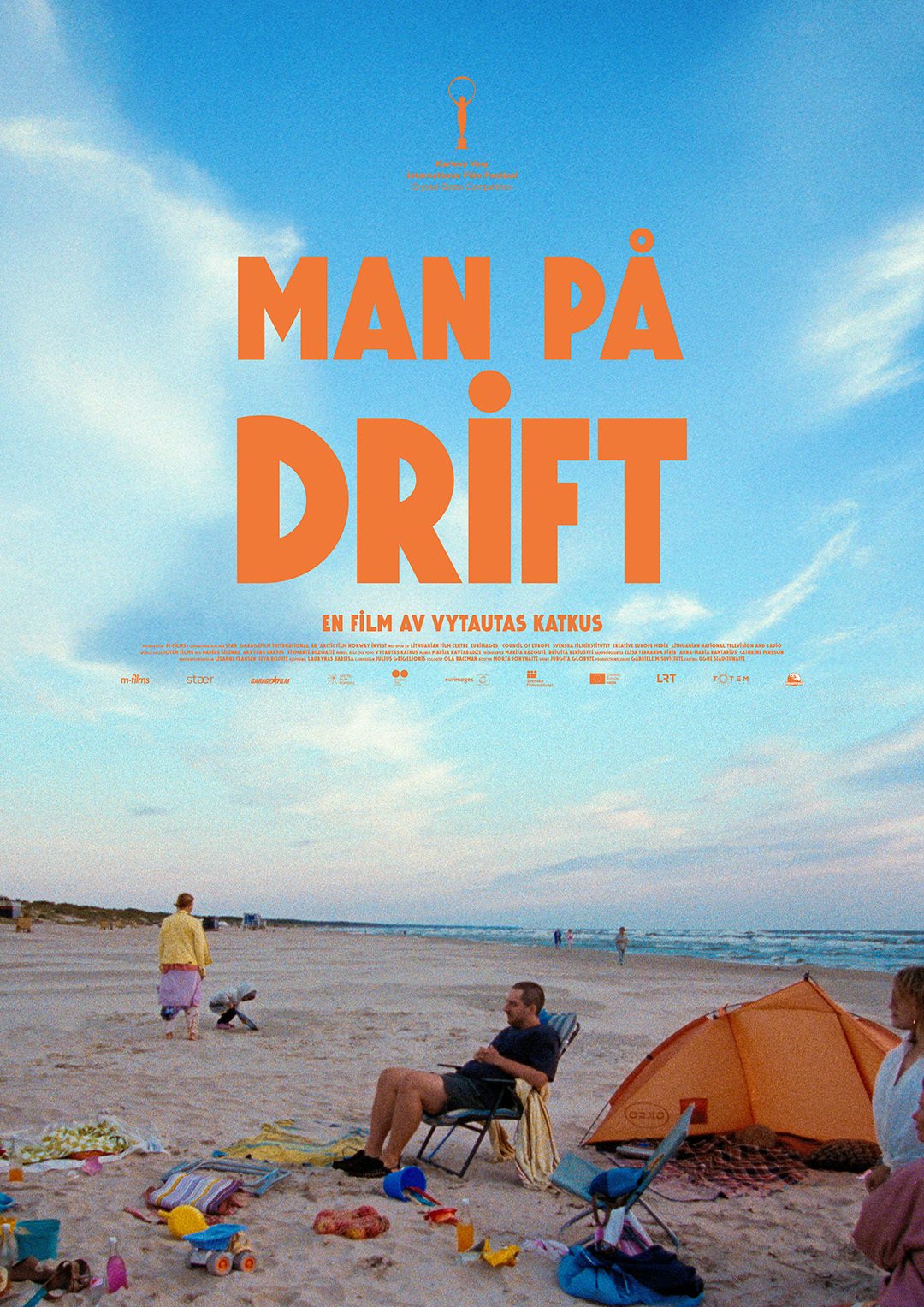 En man sitter i en solstol på en strand omgiven av leksaker i plast
